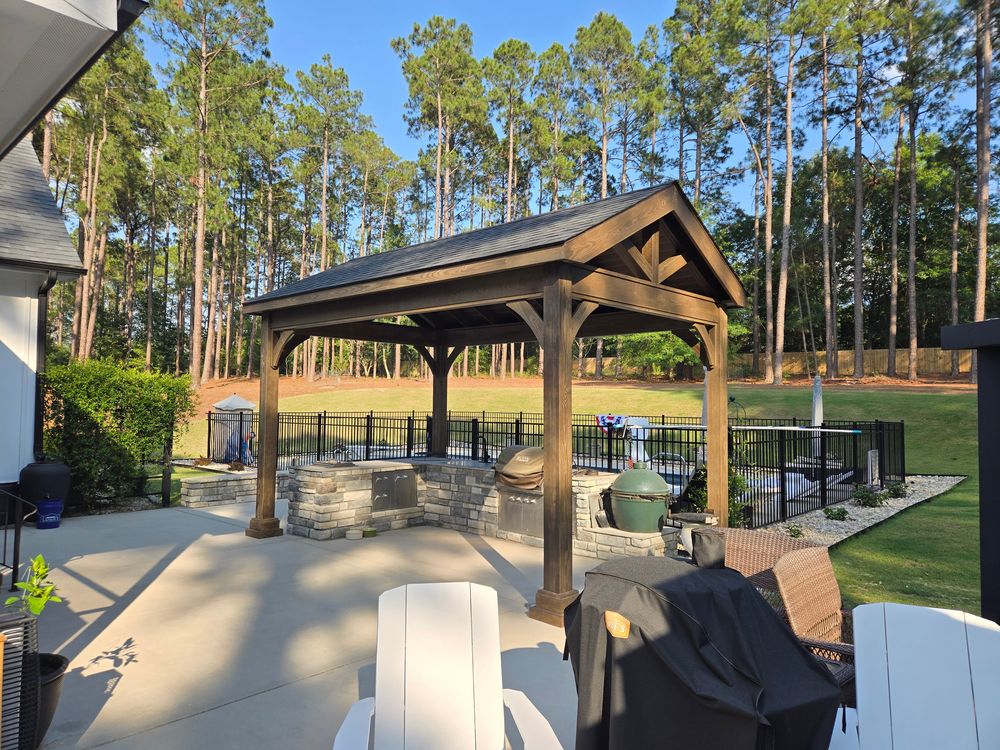 Front view of a heavy-timber gable pavilion showing the exposed truss over a stacked-stone kitchen island